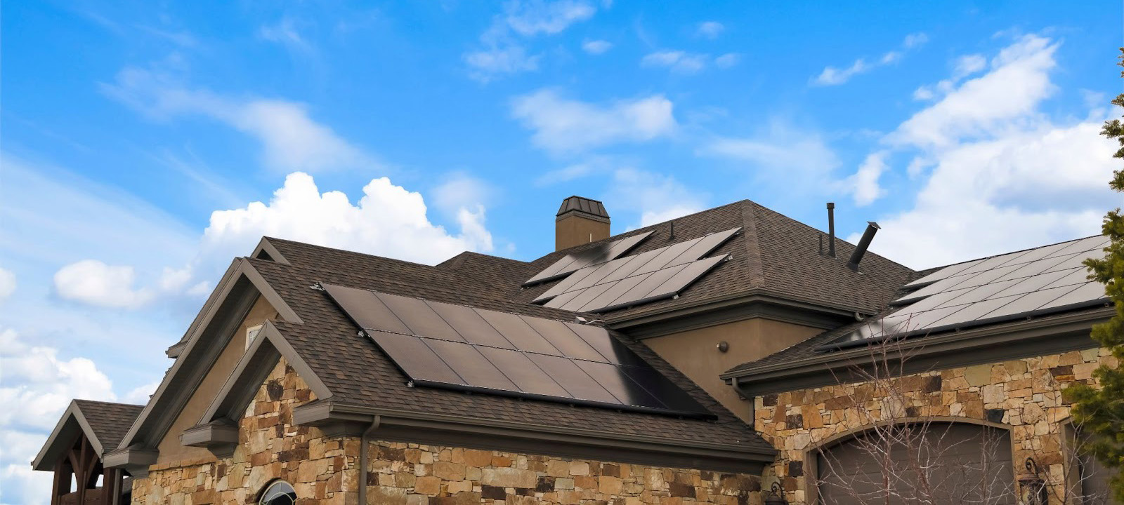 Modern stone and stucco home with rooftop solar panels in front of blue sky with white clouds, image chosen for the Enact 2023 U.S. Solar and Storage Market Intelligence Report covering residential and commercial solar projects.