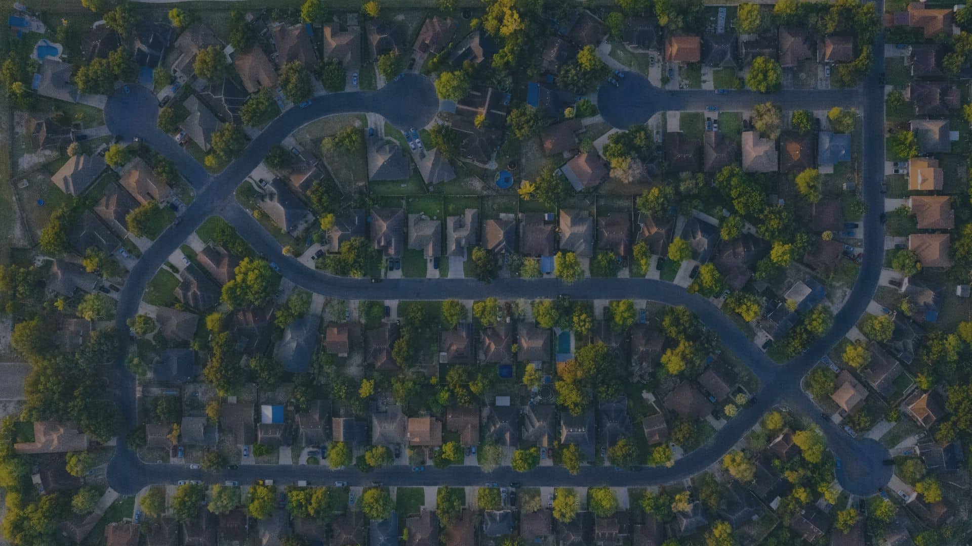 Aerial view of a suburban neighborhood with winding streets and houses surrounded by trees.